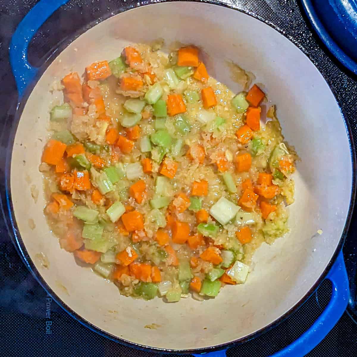 Sautéed carrots, celery, and onions in a blue pot for Curry Coconut Chicken Gnocchi Soup.