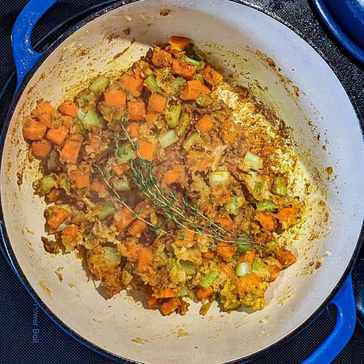 Vibrant Dutch oven filled with sautéed mirepoix, and fresh thyme for soup.