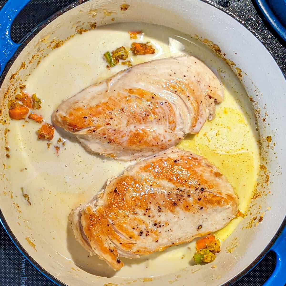 Golden seared chicken breasts in a vibrant skillet with vegetables and rich sauce.