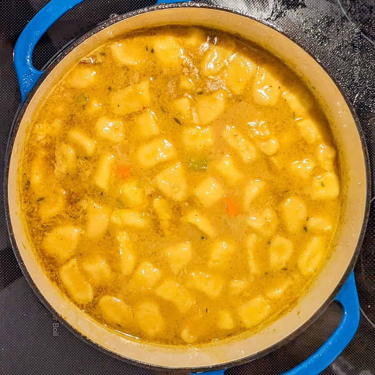 Golden curry coconut gnocchis bubbling in a blue cast iron pot.