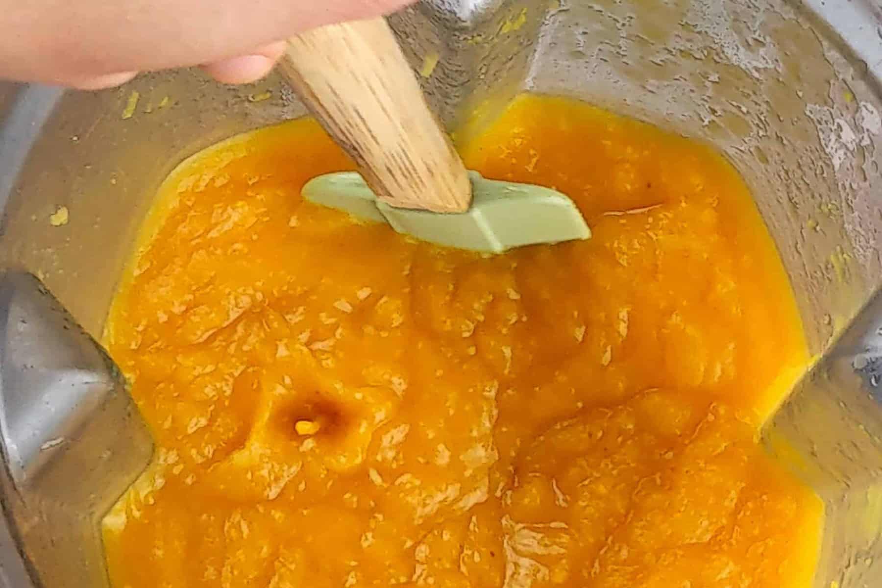 pureed roasted butternut squash in a blender container being scrapped and mixed with a silicone spatula with a wooden handle