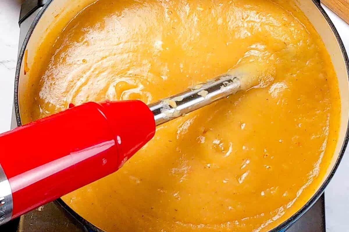 Creamy potato leek chowder blending with red immersion blender in vibrant kitchen scene.