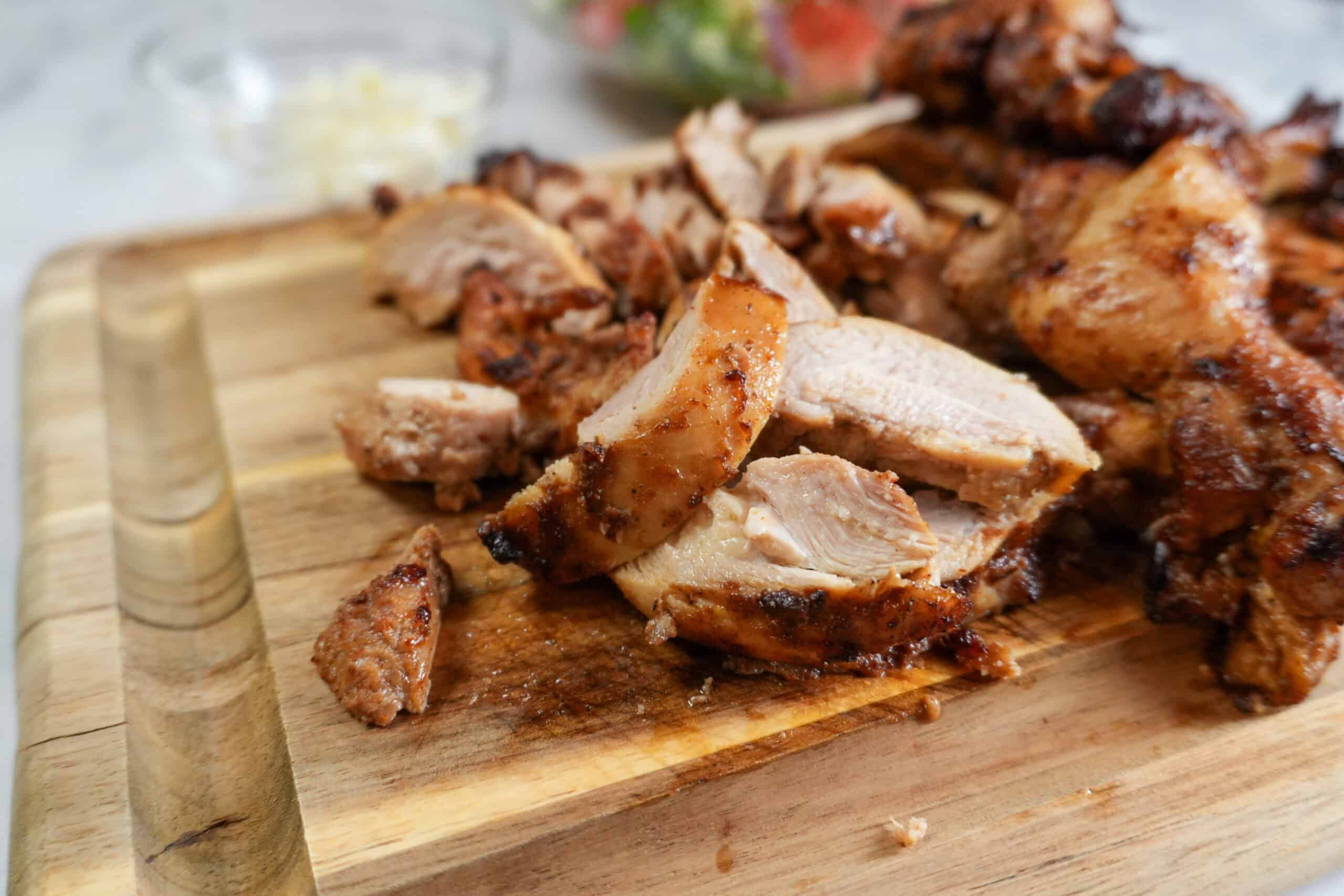 close up of the Beituti Shawarma Chicken Thighs sliced on a cutting board. with feta and cucumber tomato salad in the background.