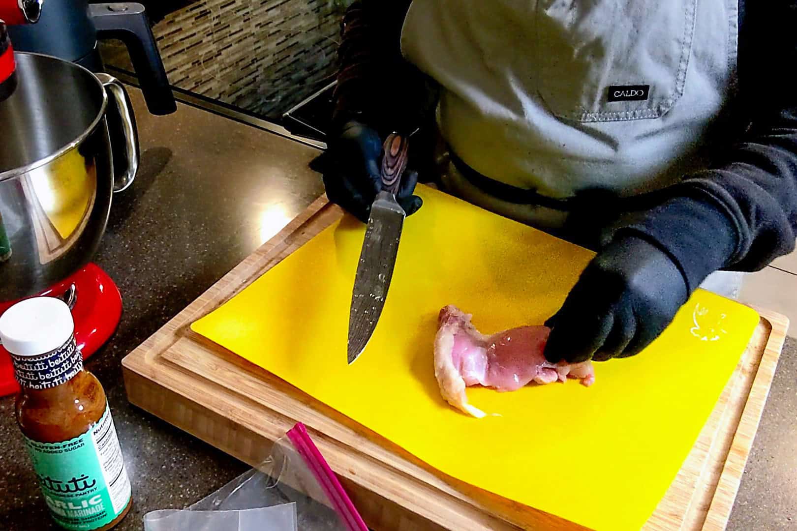 chicken thigh on a yellow plastic cutting board mat.