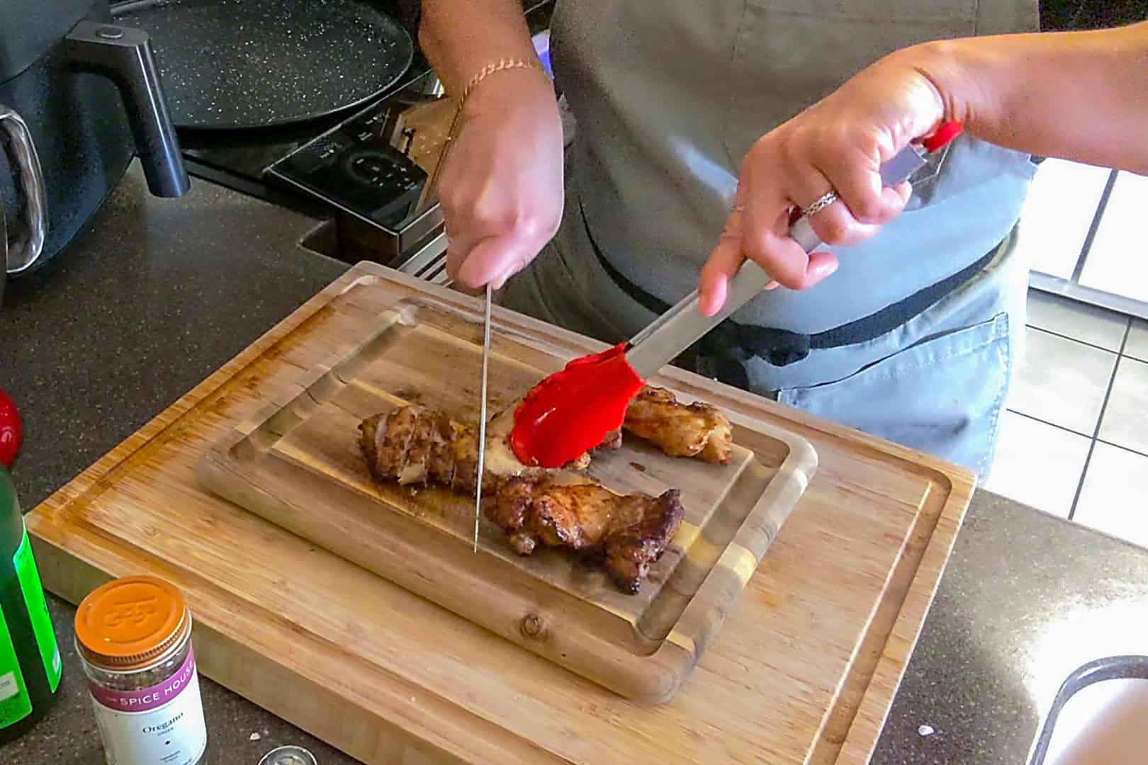 cooked chicken thighs being cut with a sharp knife with tongs hold it down.