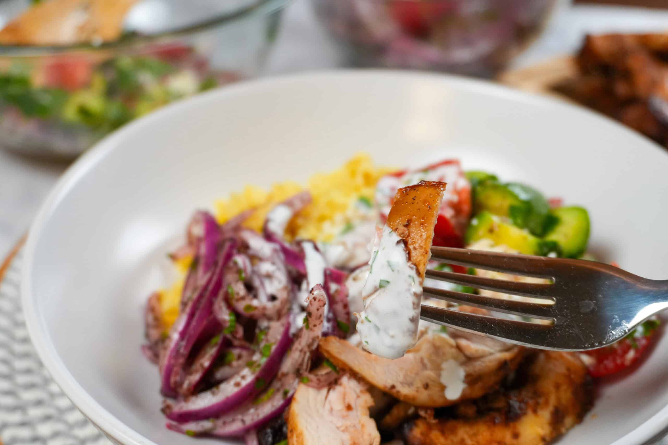 Air Fryer Shawarma Chicken Rice Bowl Beituti in a wide rim bowl with a fork and knife. with close up of the shawarma chicken drizzled with lemon greek yogurt dressing.