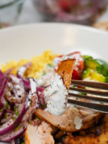 Air Fryer Shawarma Chicken Rice Bowl Beituti in a wide rim bowl with a fork and knife. with close up of the shawarma chicken drizzled with lemon greek yogurt dressing.