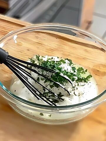 lemon greek yogurt with chopped parsley on top in a glass mixing bowl with a silicone whisk.