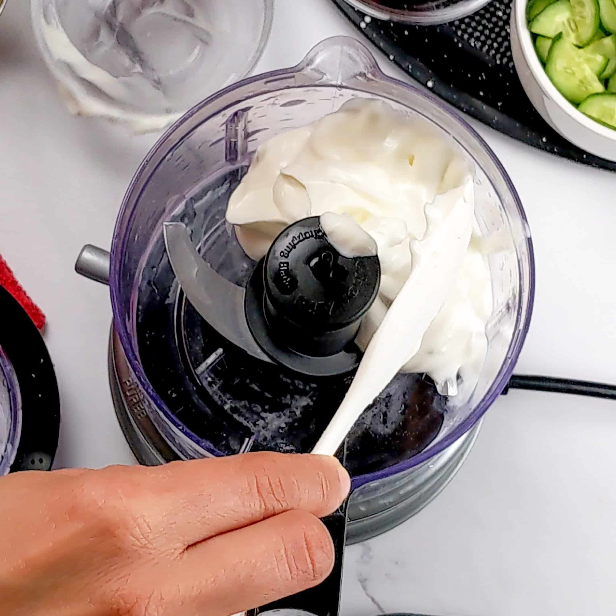 greek yogurt in a food processor with a silicone spatula.