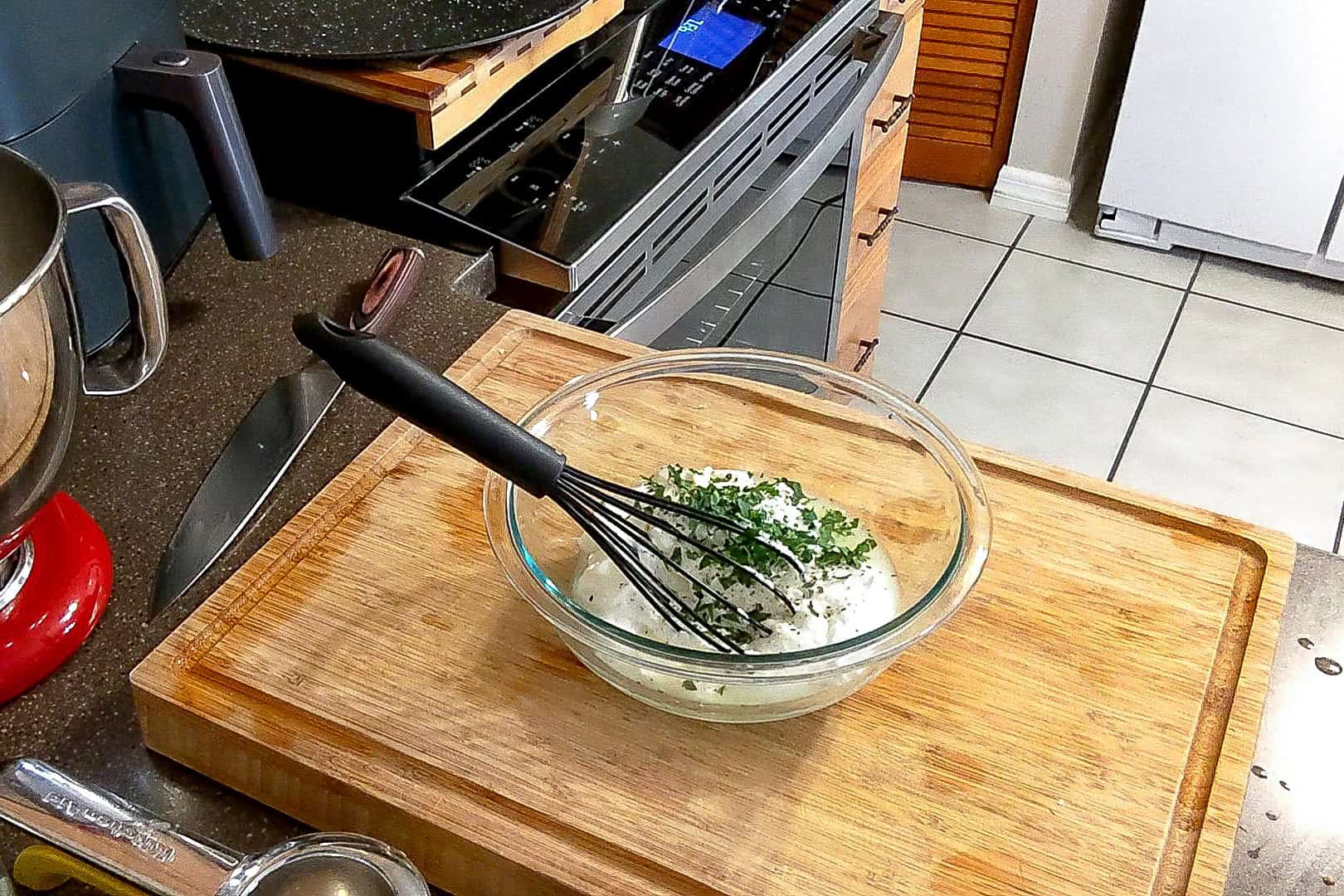 lemon greek yogurt mixture sprinkled with fresh chopped parsley sitting in a glass mixing bowl with a silicone whisk.