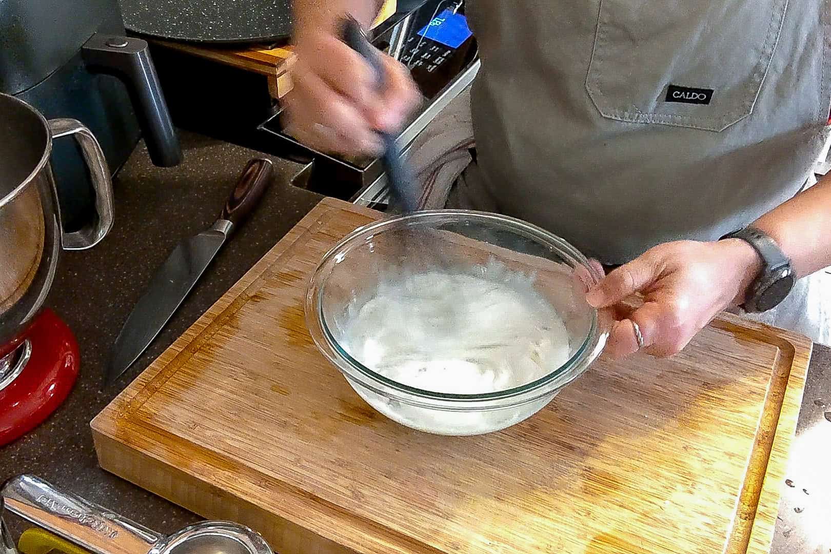 lemon greek yogurt mixture being whisked with a silicone whisk in a glass mixing bowl.