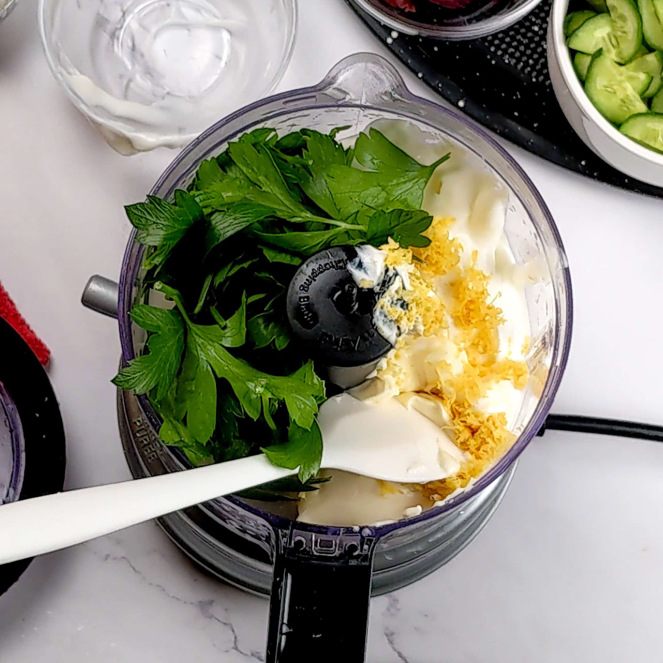 ingredients for the lemon greek yogurt dressing in a food processor with a silicone spatula resting inside.