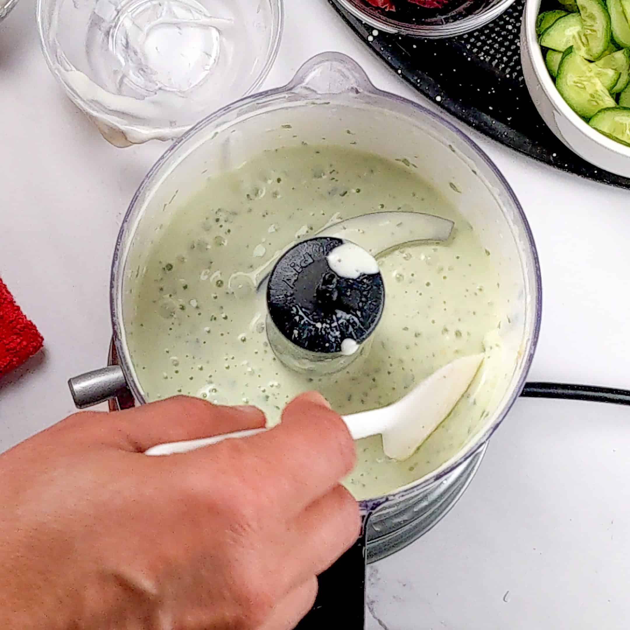 spatula testing the consistency of the creamy lemon greek yogurt in a food process with a silicone spatula.