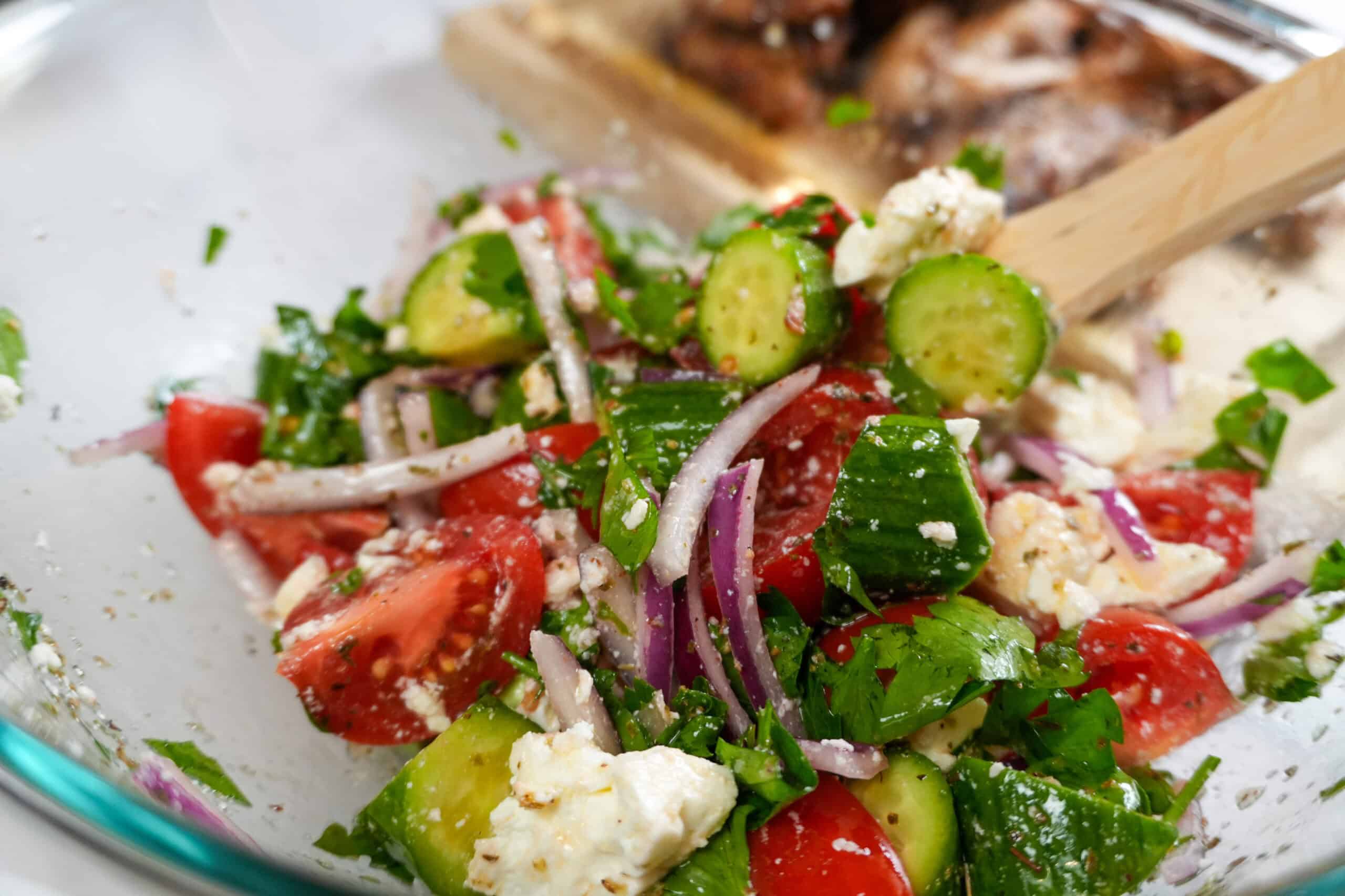 close up of the Parsley Cucumber Tomato Feta Salad in a glass bowl with a wooden spoon.