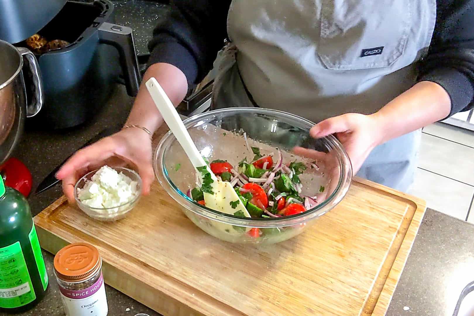 feta cheese about to be added to the cucumber tomato onion mixture in a glass bowl.