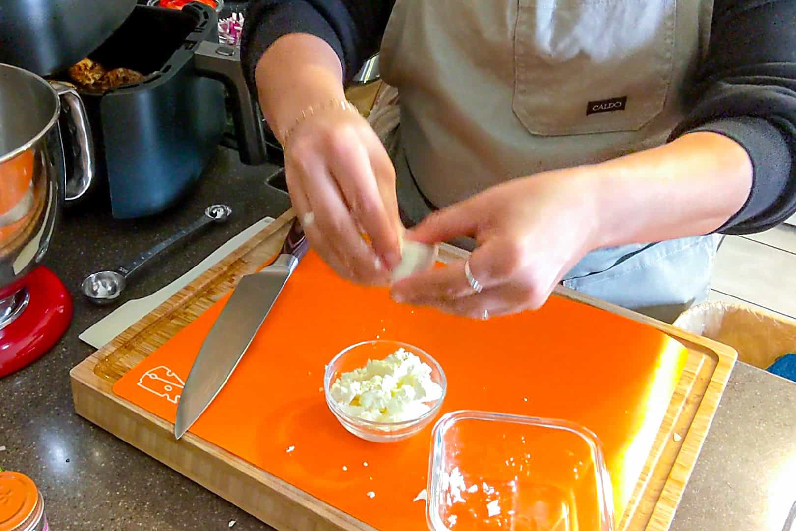 chef maika crumbled a block of feta cheese into a small glass bowl.