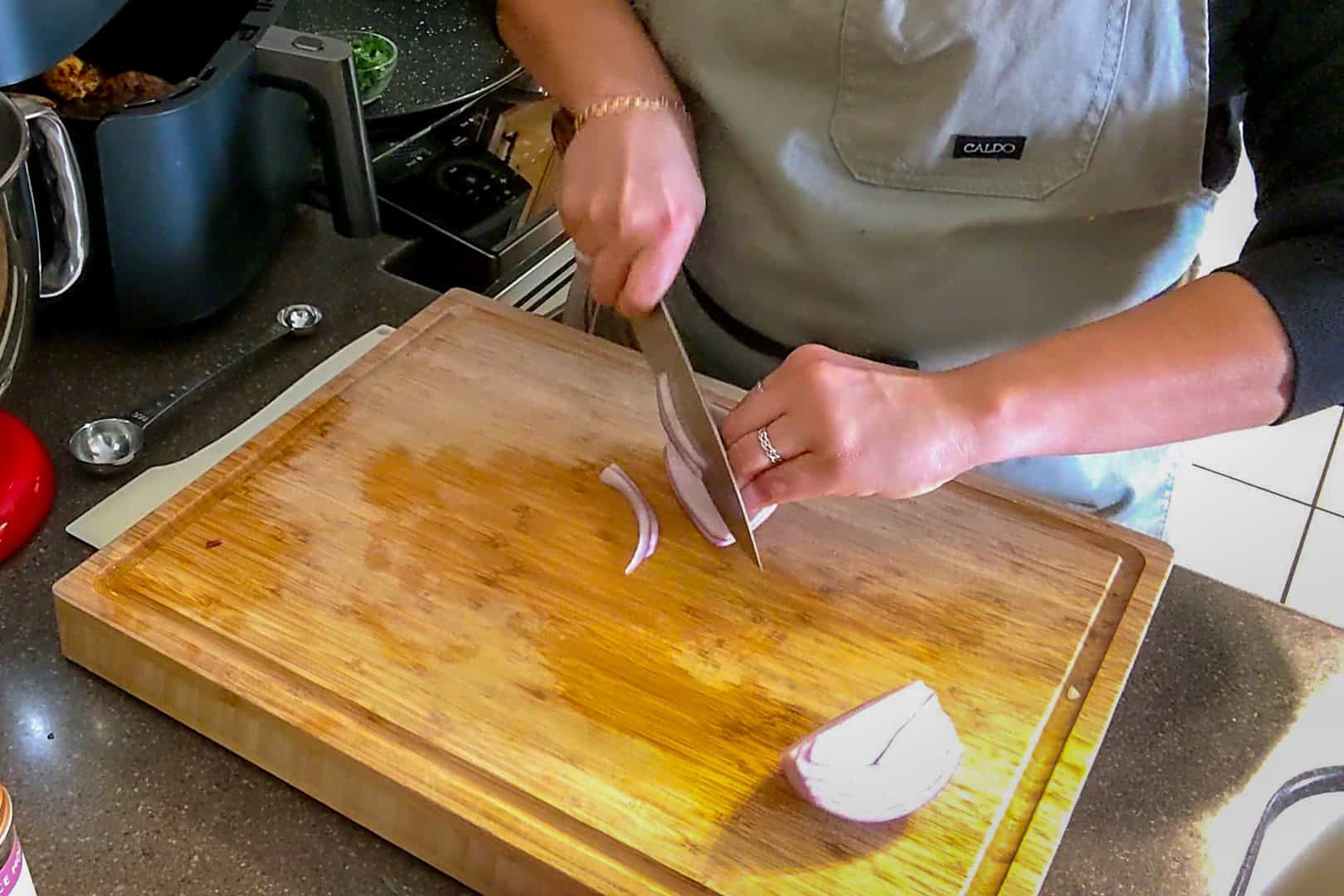 the onion being sliced on a wooden cutting board with a sharp chef knife.