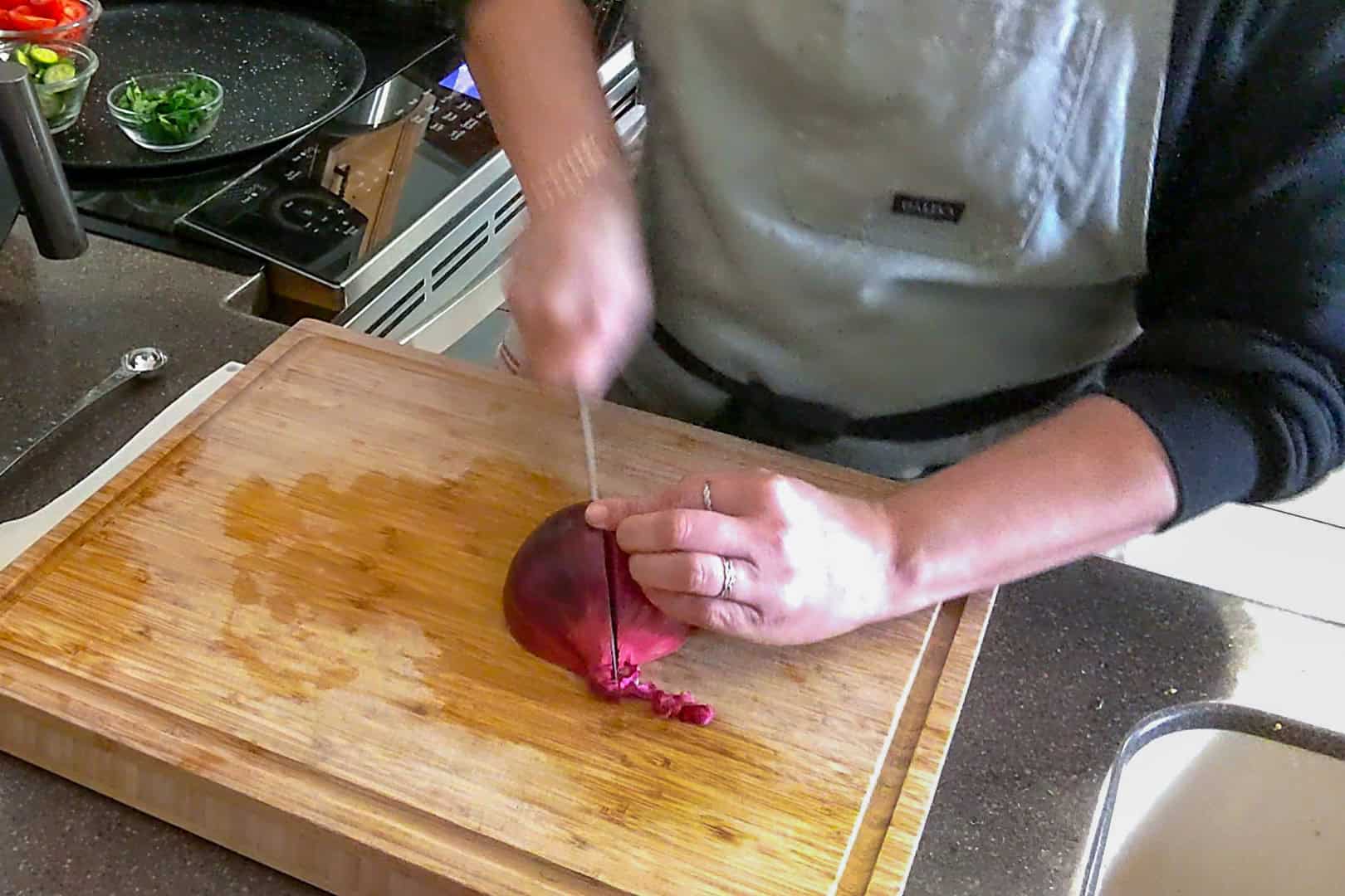 a halved red onion being cut into half again on a cutting board.