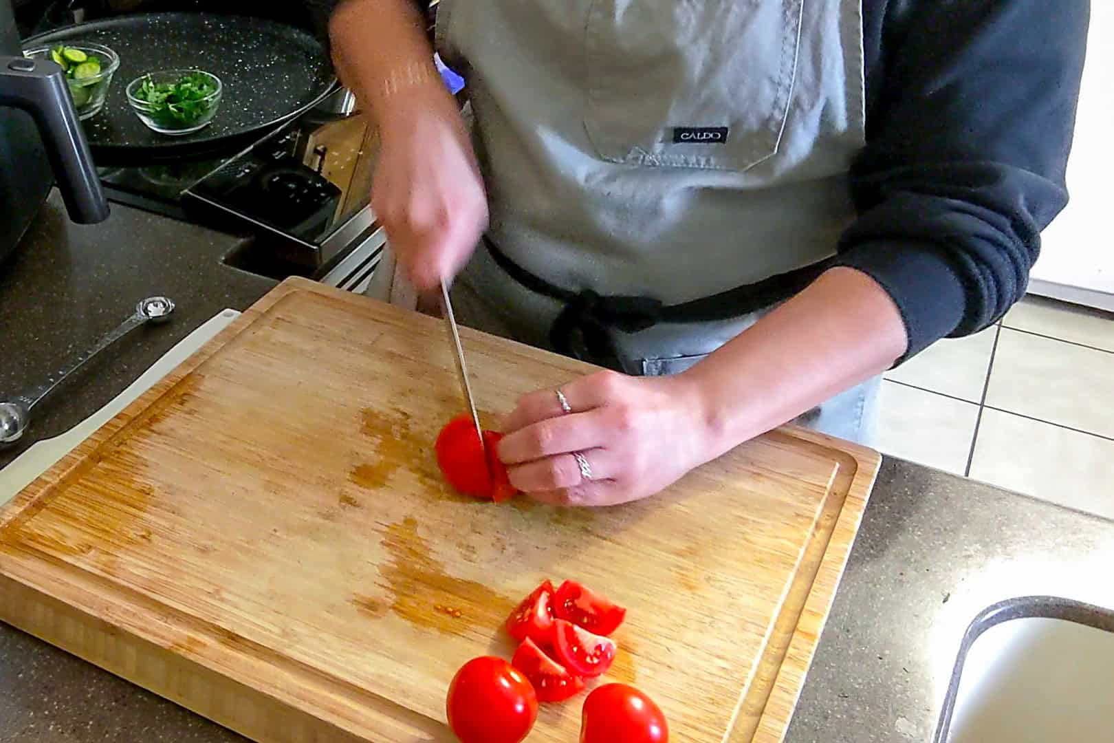 quartering campari tomatoes on a cutting board with a chef knife.