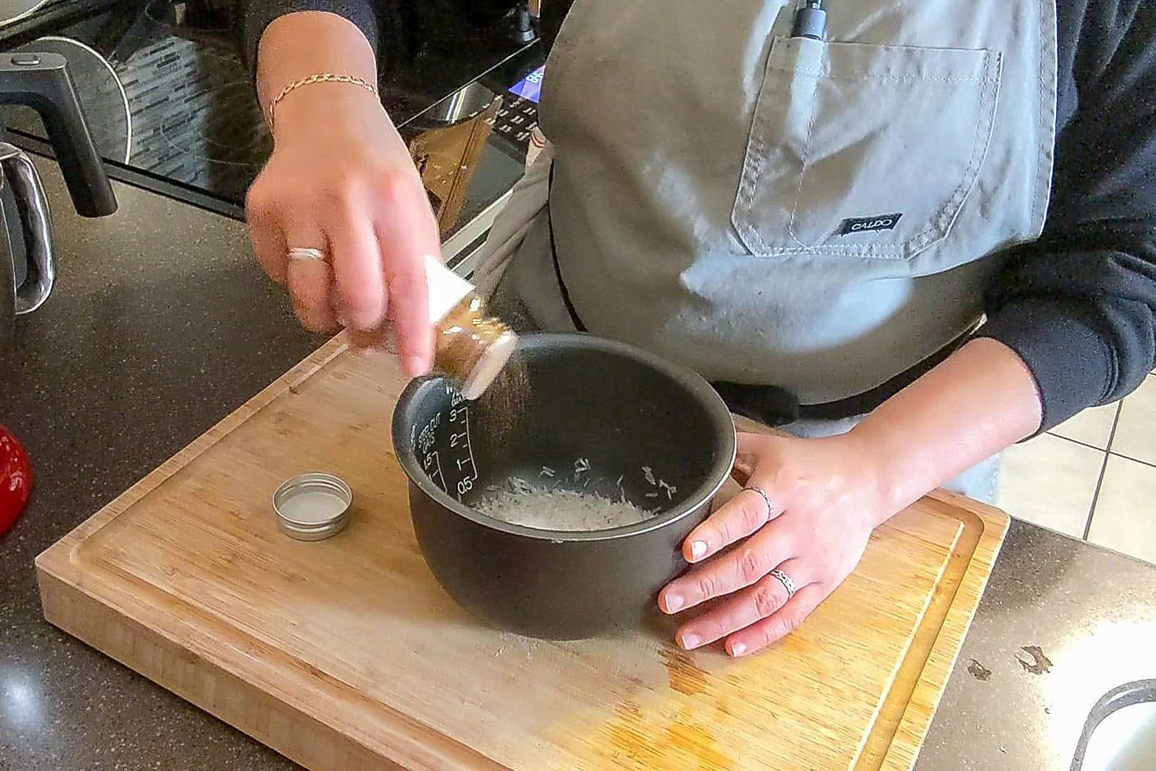 sprinkling the custom herb spice shop's spiced basmati rice seasoning blend on top of the rinsed rice.