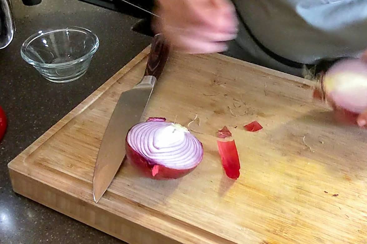 slicing a red onion in half on a cutting board with a chef knife.