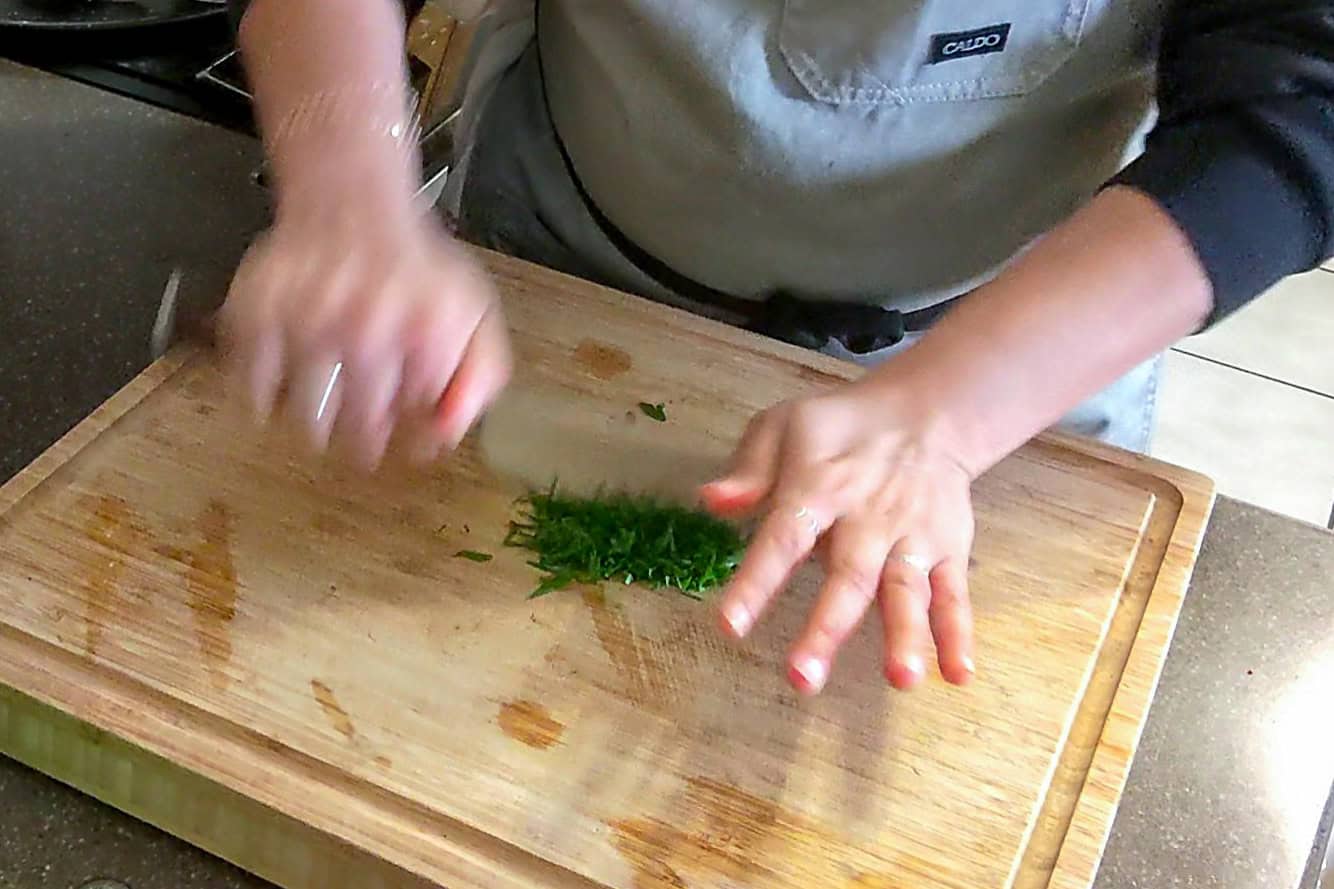 chopping fresh parsley leaves on a wooden cutting board with a paudin chef knife.