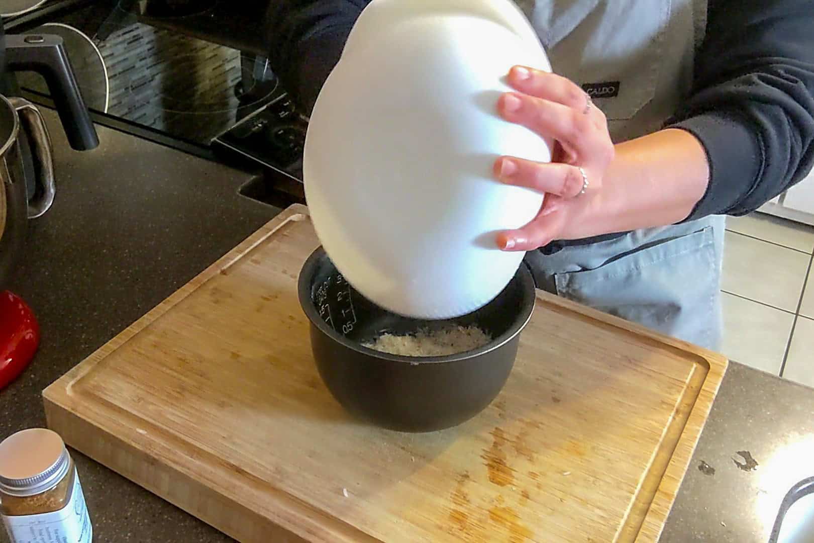 emptying out the rice from the rice washer into the rice cooker's canister.