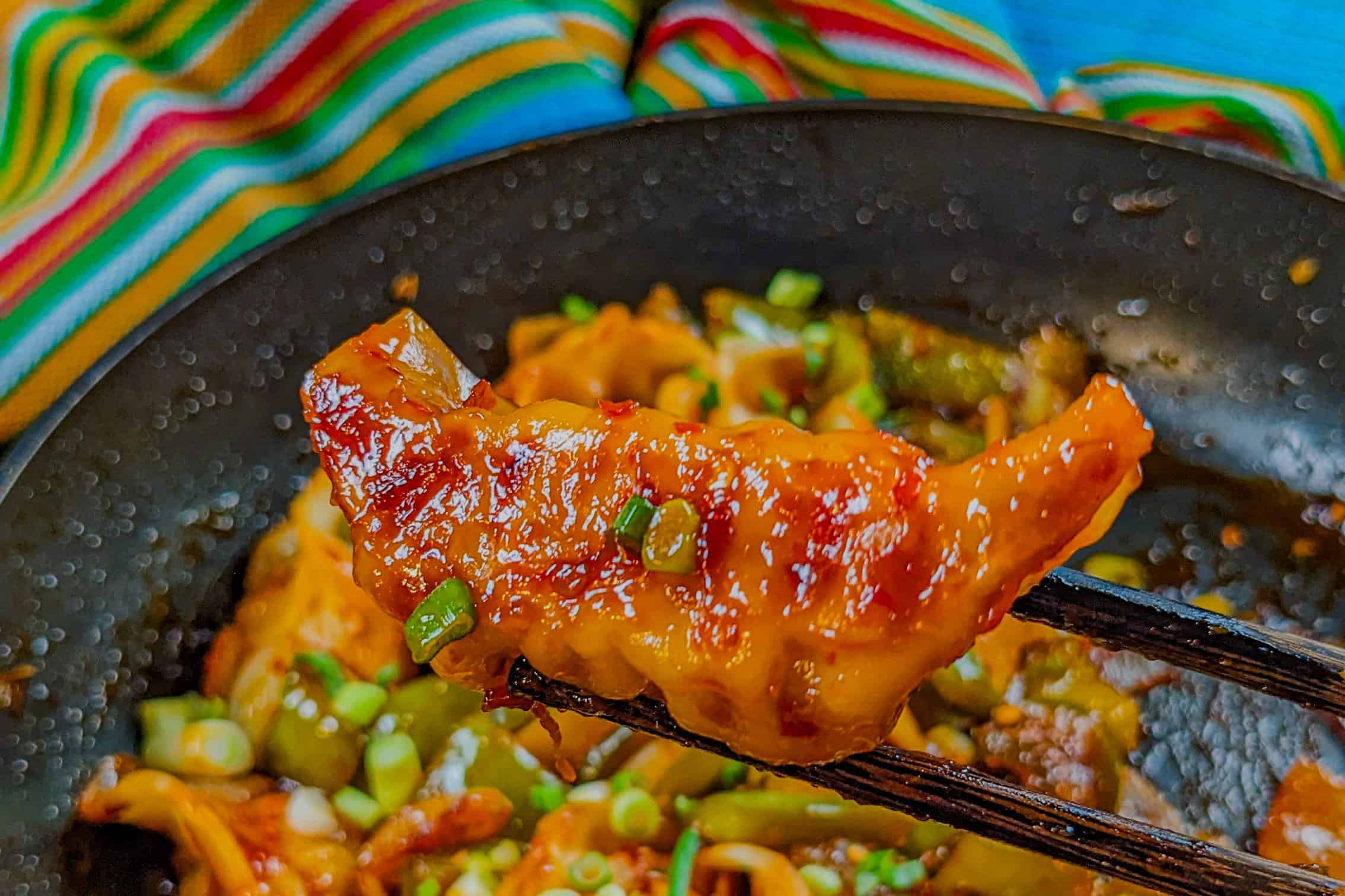 close up pan seared dumplings on chopsticks to show the golden brown bottom.