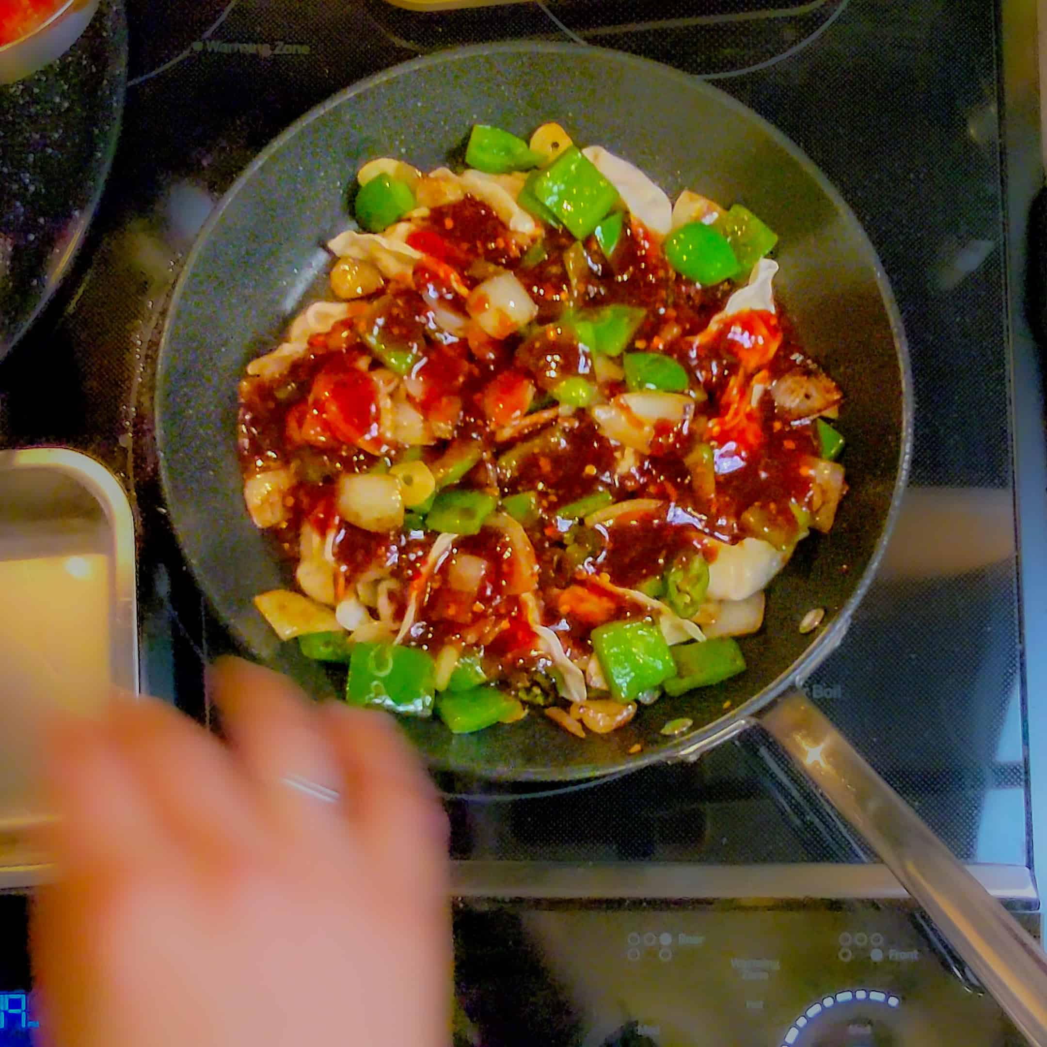 the garlic chili momo sauce poured over the dumplings and choppped vegetables in a non stick pan.