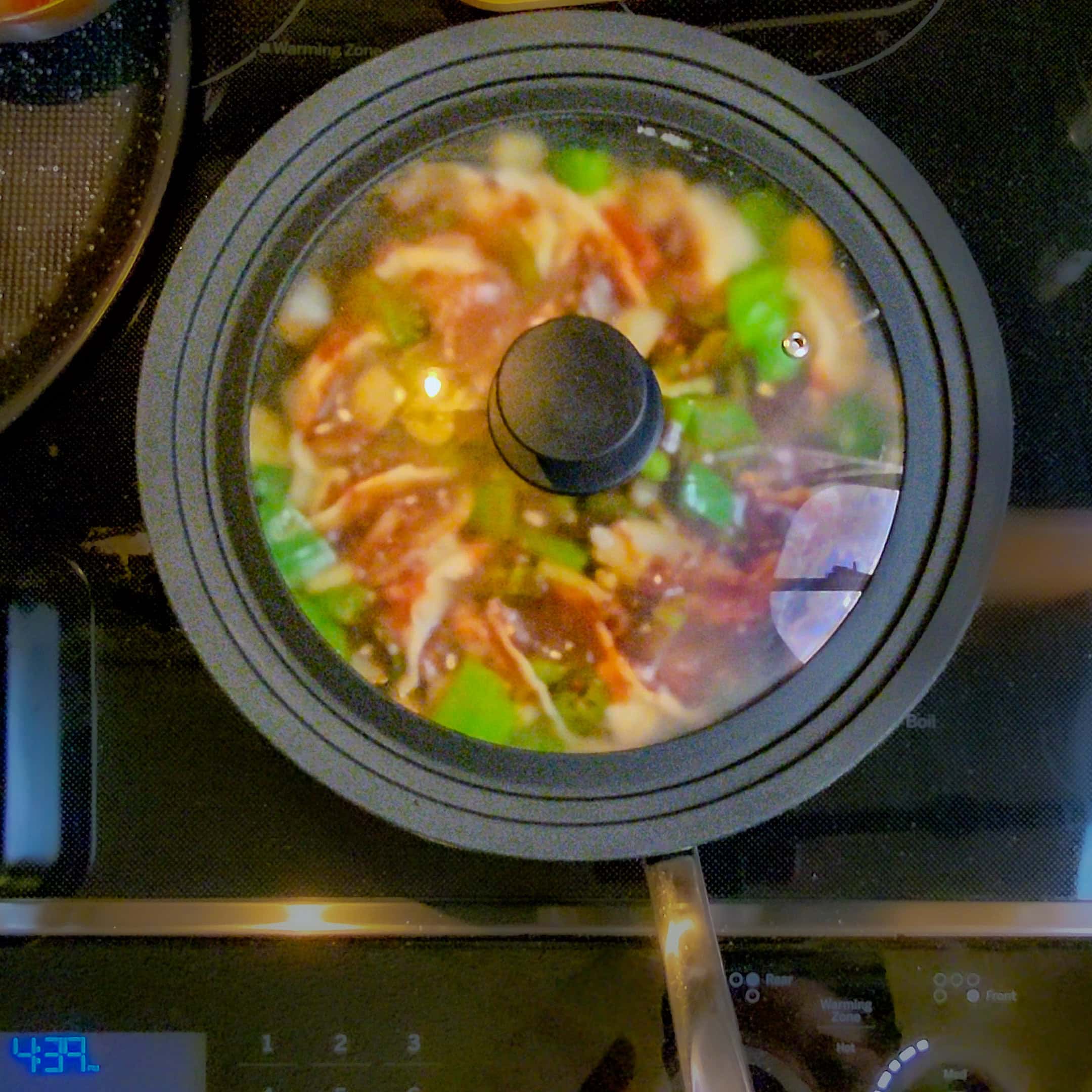 transprent lid on top of the non-stick saute pan that containes the chili momo dumplings.