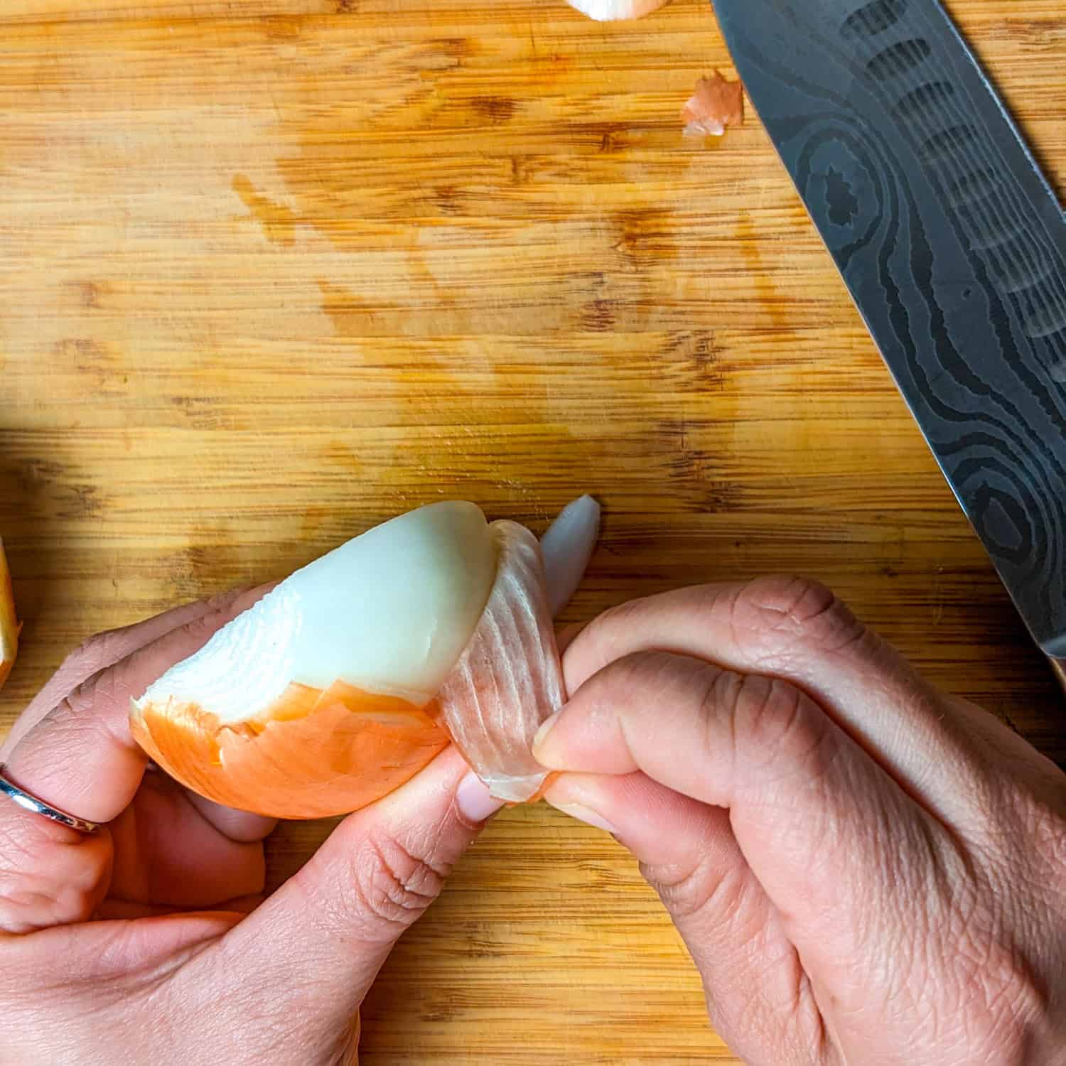 peeling a halved onion on a wooden cutting board.