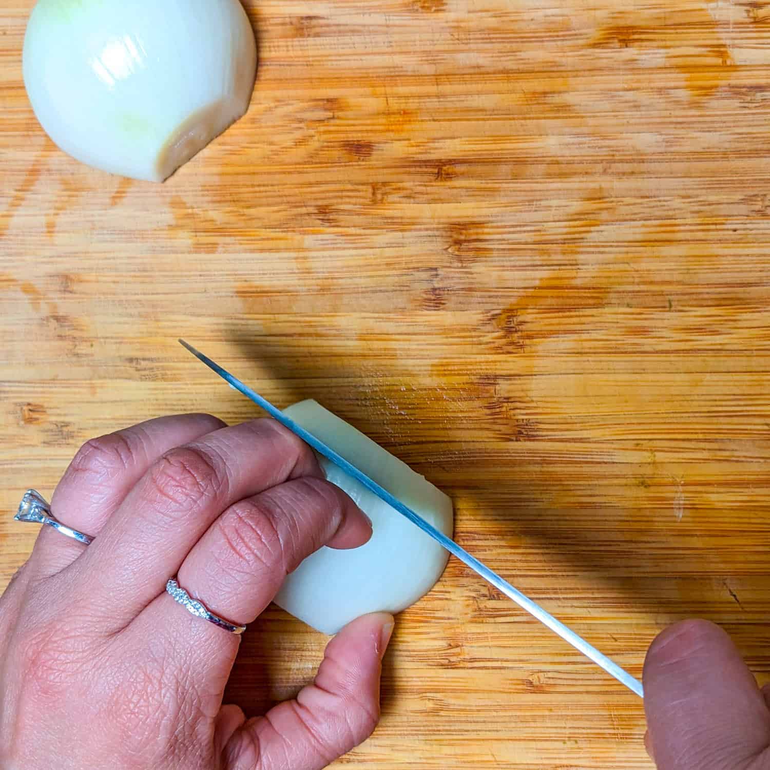 slicing the halved onion on a wooden cutting board with a sharp knife.